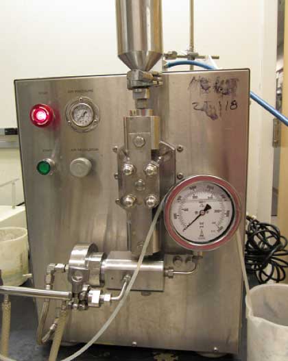 Stainless-steel high-pressure homogenizer with gauges, valves, and indicator lights on its front panel in a laboratory setting