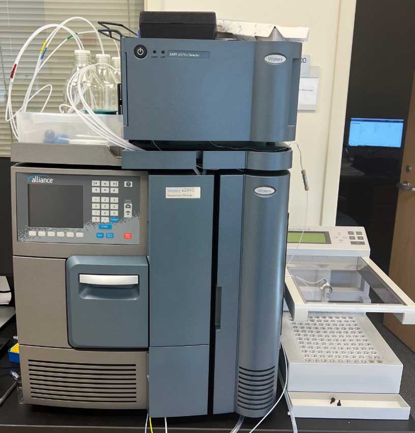 Waters Alliance H.P.L.C. system with multiple stacked modules, tubing, and an open sample tray on a laboratory counter