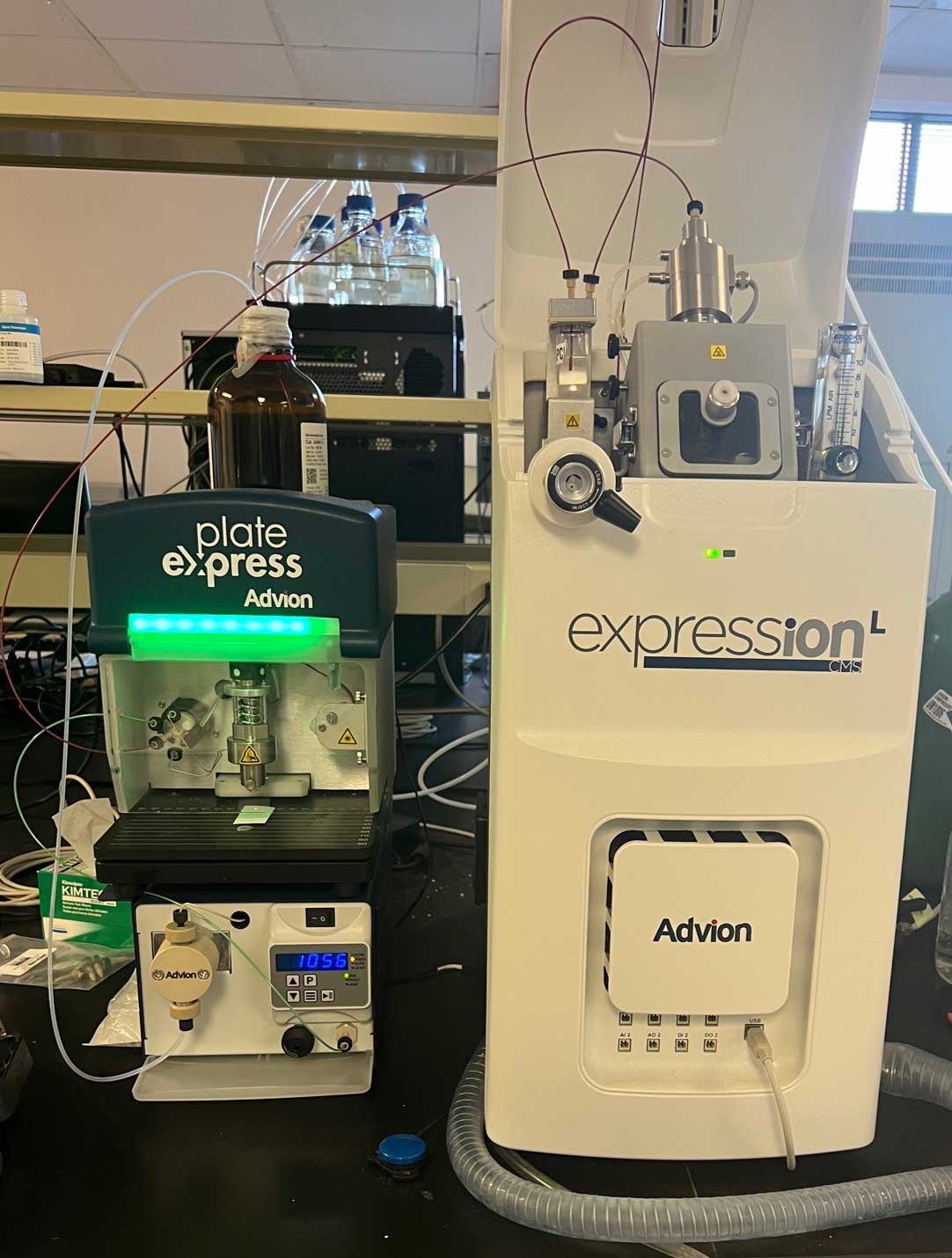 Close-up of an Advion expressionL CMS mass spectrometer system on a laboratory bench, connected with tubing and a Plate Express interface unit beside it