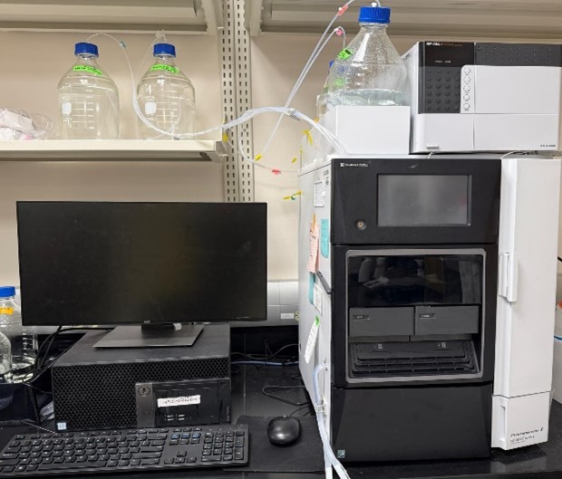Shimadzu H.P.L.C. system connected to a computer workstation, with solvent bottles on shelves above and tubing running between compon