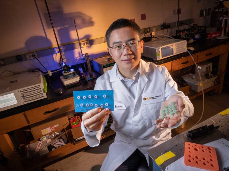 A V.C.U. researcher in a lab coat holds up samples while seated at a lab bench