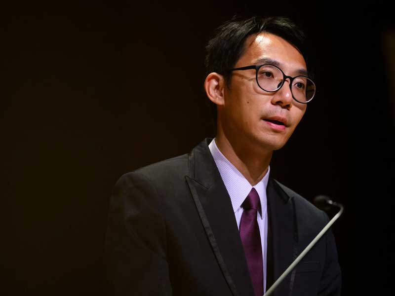 ka un lao in front of a microphone on a podium delivering a speech