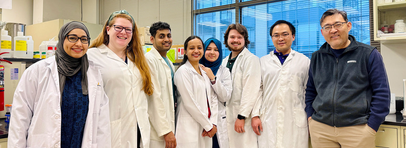 a diverse group of eight smiling people wearing lab coats in a lab